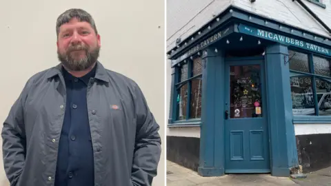 Bun X's Jeff Taylor wears a blue shirt and great coat with exterior view of Micawbers Tavern on right of frame