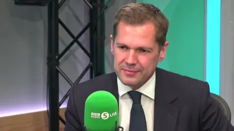 Robert Jenrick sitting in front of a BBC Radio 5 Live microphone