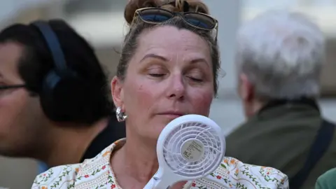 Woman holding a white fan to her face with her eyes closed.