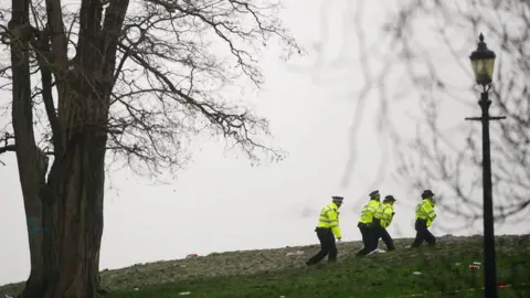 PA Media Image from January showing four uniformed police officers walking across Primrose Hill after the fatal attack, with a lamp post and tree visible in the foreground