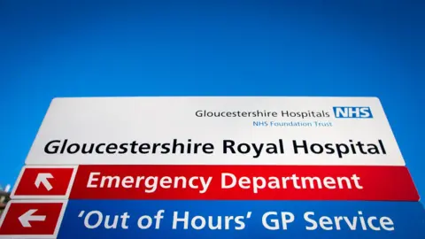 Getty Images A large sign with "Gloucestershire Royal Hospital" in black letters on a white background and underneath it directions to the emergency department and out of hours GP service.