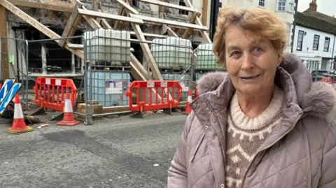 Woman in purple jacket and brown jumper stood in front of road closure scaffolding