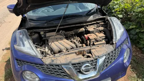 Inside the bonnet of a car on Radbourne Lane which shows the engine coated in red dust