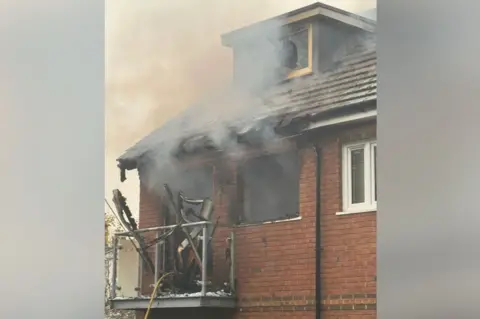 London Fire Brigade Handout from the LFB showing the house's burnt roof and smoke coming out of broken windows and debris falling off a balcony. 