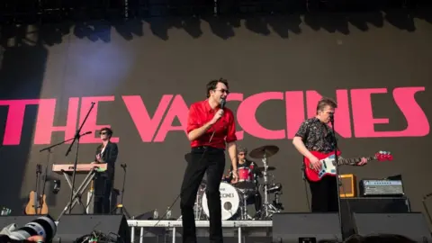 Getty Images A band consisting of a singer, bassist, guitarist and drummer, perform on stage, Behind them is a black backdrop with "The Vaccines" written in pink, capital letters.