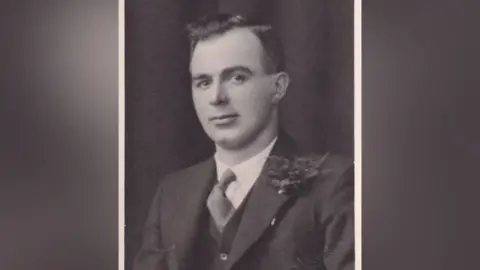 Susan Basnett Richard Roby black and white photo of man with short slicked hair, wearing a suit, waistcoat and white shirt with darker tie.