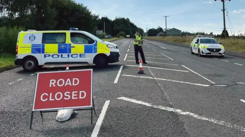 police van and car on road with road closed sign