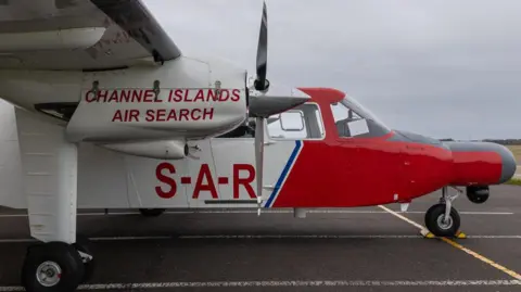 A small white and red aircraft has the words Channel Islands Air Search in red under its wing and the letters SAR, for Search and Rescue, on its bodywork.