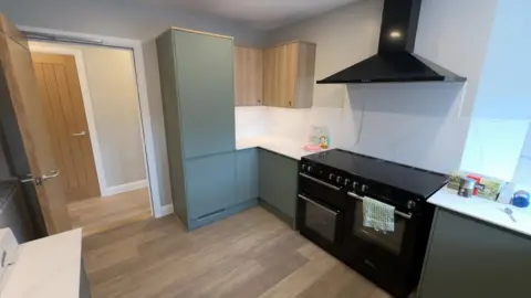 Ofsted A kitchen with pale green cabinets and a black range-style cooker and wooden floors