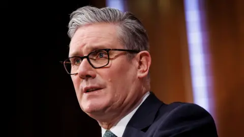 A head and shoulders shot from the side of Starmer wearing glasses and wearing a suit