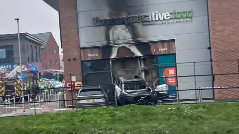 A burnt out car wedged inside a co-op food store which has also suffered fire damage.
