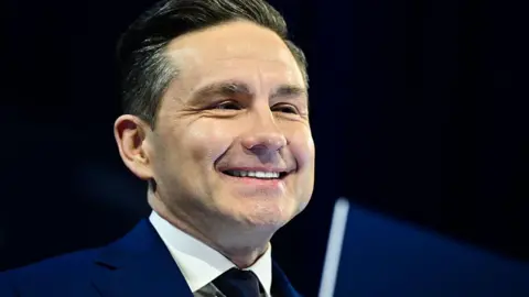 Pierre Poilievre, in a dark blue suit, smiles 