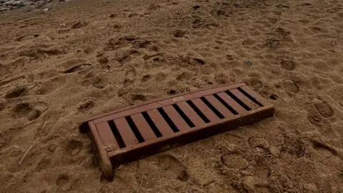 The backrest of a wooden bench lying flat on a beach, with footprints seen around it in the sand. 