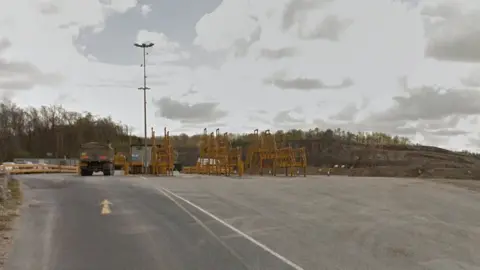 Google General view of the road leading to Leapers Wood quarry, with a lorry to the left, yellow scaffolding in the middle and the quarry rock in the background