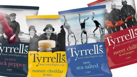 Tyrrells Four bags of crisps places next to each other on a white background. From left to right, the bags are black, yellow, blue and red.
