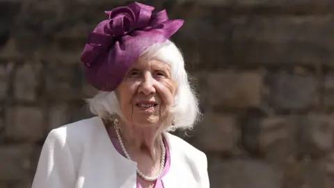 PA Media Betty Brown is staring into the camera and smiling. She has a purple flower headband on her head.