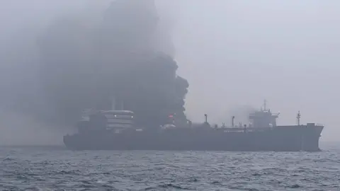 Lee Whitaker/Getty Images Black smoke pours from two large collided ships with some flames visible. In the  foreground is dark water. Some lights are on in the bridge of one of the ships. The whole scene is slightly silhouetted due to smoke in the air. 