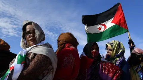 AFP Displaced Sahrawis arrive to attend a Polisario congress at the refugee camp of Dakhla, Algeria, on 13 January 2023. One of them waves the Sahrawi flag.