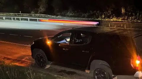 Richie Woodmason The broken down car on the M5. It is night time and there is a blown out tyre to the rear of the vehicle. The car is parked on the hard shoulder.