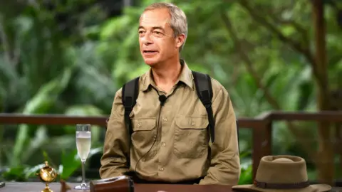 Nigel Farage sitting at a table being interviewed in the jungle