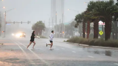 Getty Images People run across a road through the rain and wind as the outer bands of Hurricane Sally come ashore on September 15, 2020 in Gulf Shores, Alabama