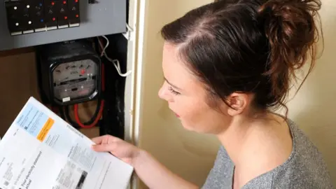 A young woman looks at an energy bill whilst taking a meter reading in her home