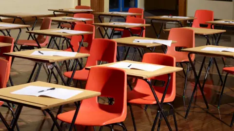 Getty Images A number of red chairs and desks in a an exam hall.