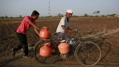 Reuters Residents push a bicycle loaded with water containers through a field in Latur