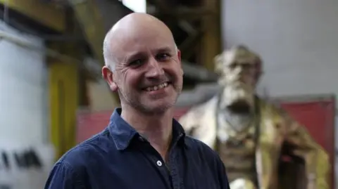 Steve Russell Studios Martin Jennings, a bald man wearing a blue shirt and grinning.