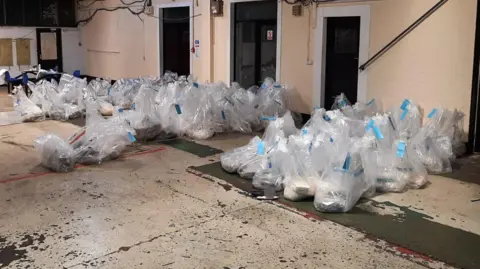 A large number of see-through plastic bags lined up in a warehouse.