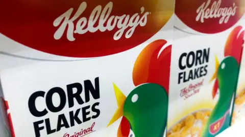 Brightly coloured packets of Kellogg's corn flakes on a shelf on a supermarket.