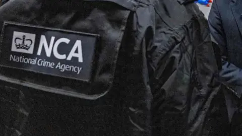 A black jacket with the letters NCA in white writing on the back and National Crime Agency underneath