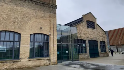 Sand Martin House is made from sand coloured brick. It has large windows and a glass entrance.