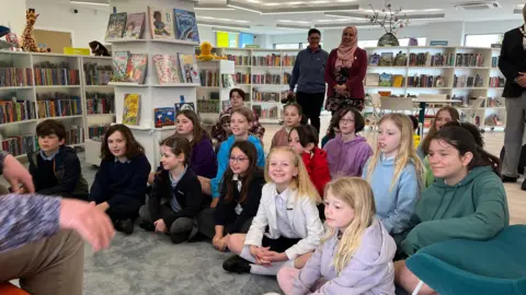 Children sat on the floor cross-legged and listening to a story inside the library.