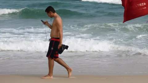 Getty Images man checking phone while walking down the beach in Brazil