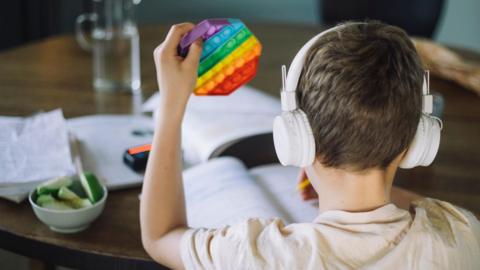 A boy wearing headphones uses a fidget toy while writing