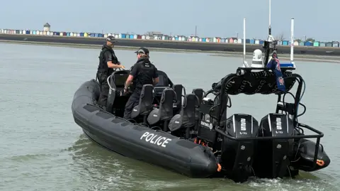 Stuart Woodward/BBC A wide shot of a black boat out on the water with the word police written along the side. Two officers are on board. 