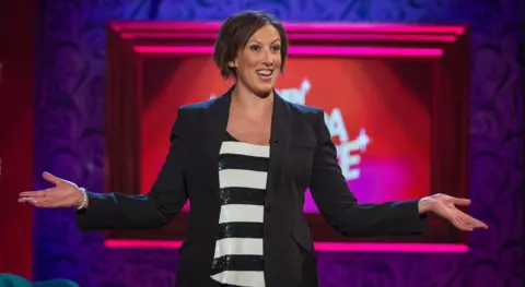 BBC Miranda Hart, pictured on the set of When Miranda met Bruce, wearing a blazer. She is smiling and gesturing with both arms, as she greets the audience.