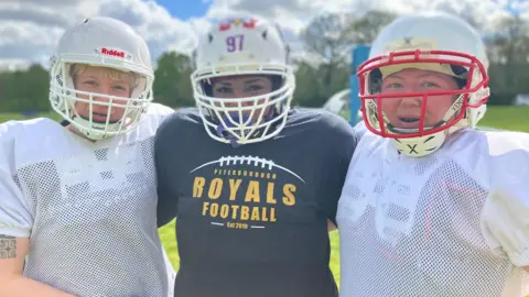 Kim, Suzie and Leila - women wearing football helmets, smiling for the camera. 