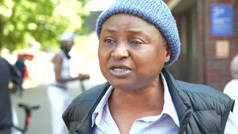 Christina Adejumo wearing a blue beanie hat, a black gilet and blue and white striped shirt.