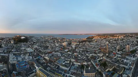 A fish eye lens view of St Hellier in Jersey showing churches housing and buildings and the sea in the background.