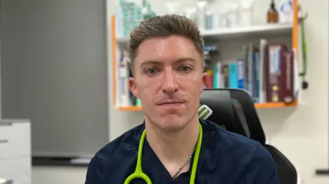 A doctor sat at his desk smiling at the camera.