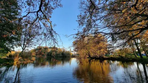 Klara Vodehnalova Lake with the reflections of the trees and a blue sky in the background.