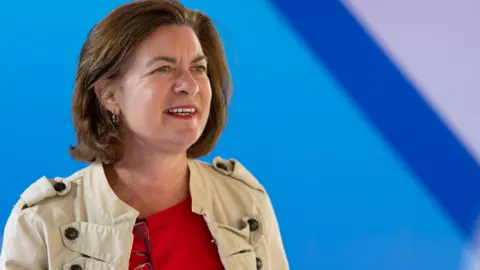 Getty Images Eluned Morgan looks into the distance. She is wearing a red top and a fawn military style jacket. Behind her is a blurred blue background.