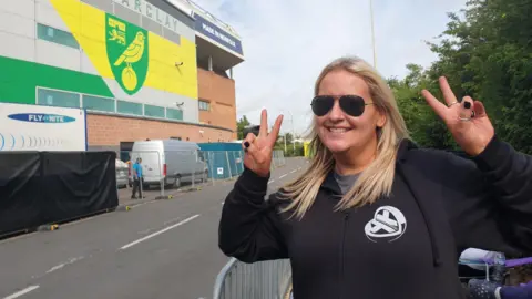 Robby West/BBC Gemma Clark in a black hoodie smiling outside Carrow Road