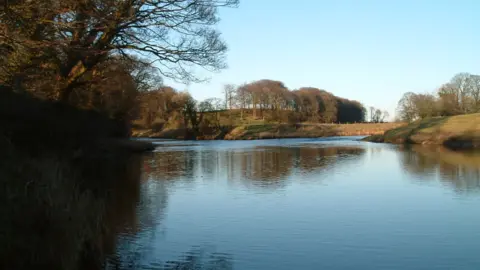 Sunset over the River Hodder surrounded by green and brown banks and trees