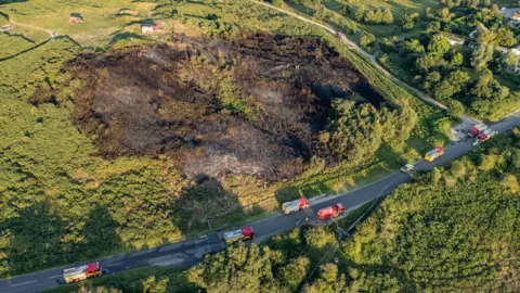 Aerial view of a burnt area of heathland surrounded by fire service vehicles