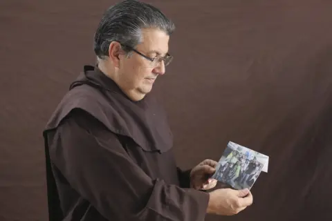 Caritas Father Cristóbal Domínguez holds up a photo of youth from hs parish