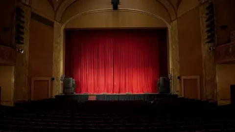 Getty Images A view of a red curtain on the stage of an empty theatre