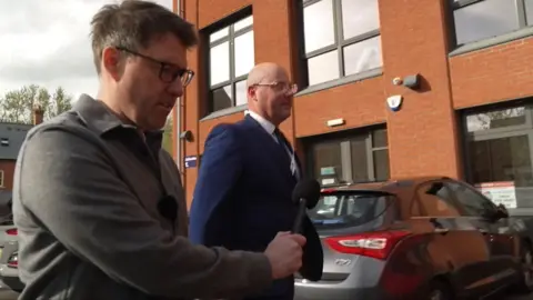 A BBC reporter is following a councillor through a car park